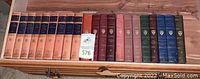 Photo showing the full collection of 18 Harvard Classics books arranged on a wooden surface; various spine colors and gold text present.