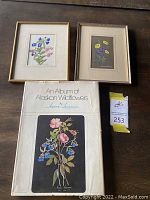 Lot showing two framed botanical prints and one book by Jeanne Laurence on a wooden surface.