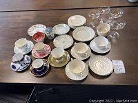 Full view of 6 tea cups each with a matching saucer, 6 unbranded saucers, 4 clear sherbet glasses, 1 clear dessert/sherbet glass with striping, and a sugar dish with lid on wooden table.