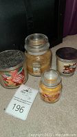 Photo showing four used candles on carpeted floor, including Bath and Body Works Spiced Gingerbread scent and Yankee Candle with glass lids and metal lid candle.