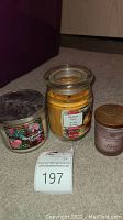 Three miscellaneous used candles displayed on carpet: Bath and Body Works Marshmallow Fireside, Ashland Golden Poinsettia, Chesapeake Mind and Body small candle