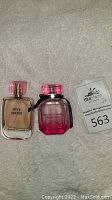Two perfume bottles side by side on a textured light carpet. Left bottle labeled Sexy Secret Jean Marc Paris, right bottle Victoria's Secret Bombshell with pink ombre and black ribbon.