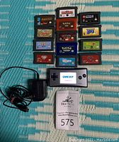 Overview of silver Game Boy Micro, charger cable, and 13 GBA cartridges on woven mat