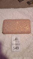 Front view of rectangular pink glitter wallet lying flat on a white textile surface with auction number card beneath.