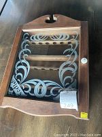 Front view of antique wooden wall hanging pipe cabinet showing etched glass door with decorative patterns and 'pipes' text, wood frame with rounded top and knob.