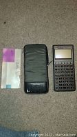 Photo showing the HP 48SX calculator with manual and black zippered case laid out on carpet.