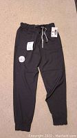Full view of black scrub jogger pants laid flat on carpet, showing elastic waistband, tie, and ankle cuffs.