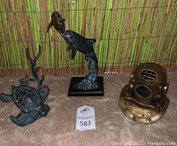 Photo of all three sculptures: bronze sea turtle, dolphin sculpture on wood base, and antique brass diving helmet.