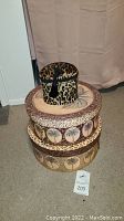 Four round storage containers stacked: small leopard print box on top of three larger palm tree theme boxes with various decorative edges.