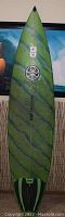 Full length front view of green swirled Hawaiian Island Creations 7'2" funboard surfboard showing pointed nose and Dakine stomp pad with FCS fins attached.
