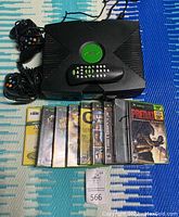 Photo of original Xbox console, two wired controllers, remote control, and 10 game cases.