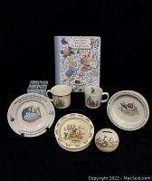 Full lot of Bunnykins set items arranged with cups, bowls, piggy bank, pencil holder, and recipe scrapbook.