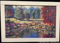 Framed art print showing a colorful pond scene with trees, rocks, and flowers, surrounded by a white frame.