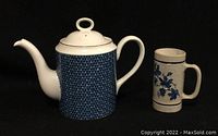 Blue and white ceramic teapot with blue textured pattern and a floral design mug on a black background