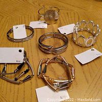 Overview of 6 brand new bracelets on table with original price tags visible. Varied styles and materials, some with metal tubes, beads, and textured metal pieces.