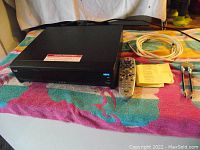 Black Bell Model 9241 HDTV receiver and remote control, coaxial cables, instruction sheet displayed on colorful towel.