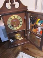 Close-up of open mantel clock showing clock face, pendulum and winding key inside the wooden case with open glass door.
