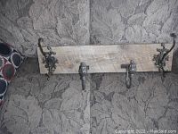 Full view of rustic wood coat rack with four metal hooks on a patterned fabric surface