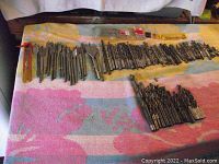 Wide view showing a long line of drill bits and spade bits laid on a multicolored fabric, displaying quantity and size variety.