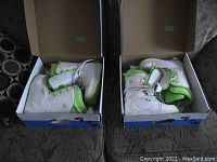Two pairs of white and green young girls' snowboard boots sitting in their boxes, showing both left and right boots from an angled top view.