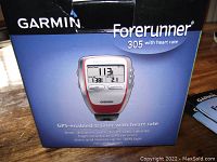 Box shows Garmin Forerunner 305 with heart rate, features printed including time, distance, pace, heart rate, calories, GPS receiver, memory for up to 1000 laps, no calibration required.