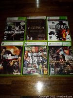Six Xbox 360 game cases laid out on wood floor, showing front covers including Call of Duty Black Ops Combo Pack, Oblivion GOTY, Battlefield Bad Company 2 Ultimate Edition, Dead to Rights Retribution, Grand Theft Auto IV, Dragon's Dogma.