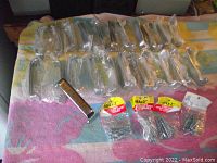 Wide photo showing 22-24 chrome stainless steel drawer/door handles individually wrapped in plastic, laid out on a colorful towel. Small packages of M4x2 inch mounting screws are also included.