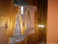 Photo showing 4 large metal hinges resting on wooden surface, varying finishes visible