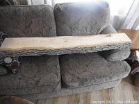 Full view of the live edge ash wood slab resting on a floral patterned couch, showing the overall length and thickness with bark along the edge.