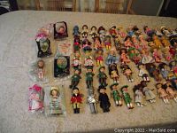 Overview photo showing a large arrangement of approximately 45 vintage McDonald's collector dolls lying on a fabric surface with various outfits and styles.
