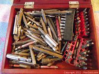 Large wooden box open with many metal drill bits including Philips, flat, and torque bits in various sizes. Some bits are stored in black and red plastic holders.