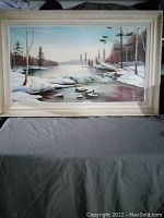 Framed painting on board showing a winter lake with trees and rocks covered in snow. The signature 'Breen 64' is faintly visible in the lower right.