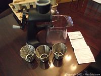 Main Pampered Chef food grater unit, three stainless steel drum attachments, clear plastic catcher container, instruction manual, and original packaging on table.
