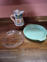 Full set including pottery jug, green Fire King pie plate, clear Fire King pie plate on wooden surface.