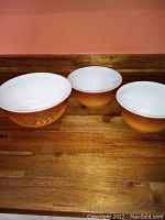 Three Pyrex Old Orchard mixing bowls arranged side by side on a wooden surface showing size differences and exterior pattern.