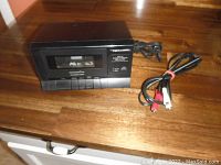 Front view of Realistic SCP-31 cassette player showing cassette compartment window and attached RCA cables on wood surface.