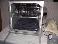 Showtime Rotisserie & BBQ oven interior open door showing rotisserie spit rod, drip tray and basket inside.