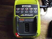 Top view of Ryobi 12 volt lithium battery charger with red indicator light lit beside charging cradle.