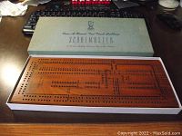 Top-down view of the wooden Scoremaster cribbage board inside its original box with visible holes and engraved markings.
