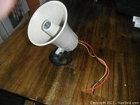 White horn-style siren speaker on wooden surface with black mounting bracket and red, yellow, black wires.