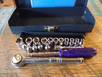 Metal case open showing ratchet, extension bar and 20 chrome sockets organized inside.