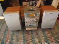 Front view of Sony micro hi-fi system including central unit and two speakers on either side, placed on a textile surface indoors.