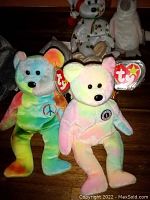 Two Ty Beanie Babies, colorful tie-dye bear and pastel rainbow bear, both with Ty tags attached.