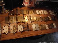 Wide shot showing multiple rows of vintage door hinges in varying conditions and finishes laid out on a wooden surface.