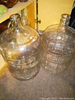 Two large clear glass wine carboys placed side by side inside a cupboard area.