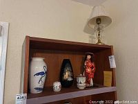 Wide shot showing the wooden shelf holding all three Asian decor items and the metal lamp on top.