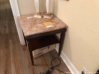 Square vintage side table with marble top, placed against wall on hardwood floor.