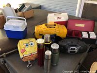 Full view of lot items including coolers, thermal jugs, Cool Tunes signed cooler, boombox, and 8-track tapes in case.