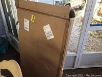 Photo of large flat cardboard box sealed, labeled with shipping stickers showing the crate is unopened.