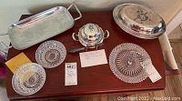 Top-down view showing all silver pieces on the table: Forbes sterling butter dish with lid, Meriden S.P. covered serving dish, rectangular silver tray, glass candy dishes, and a note